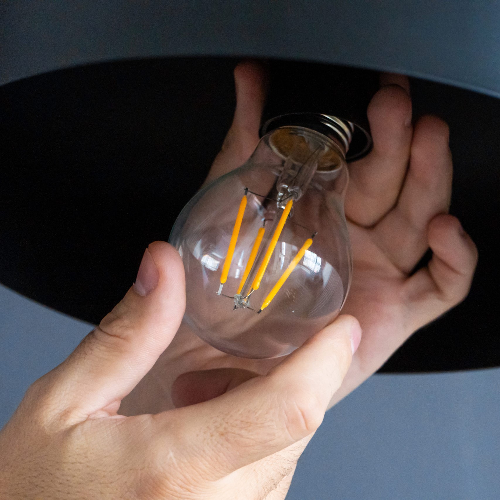 Close-up. A hand changes a light bulb in a stylish loft lamp. Spiral filament lamp. Modern interior decor.