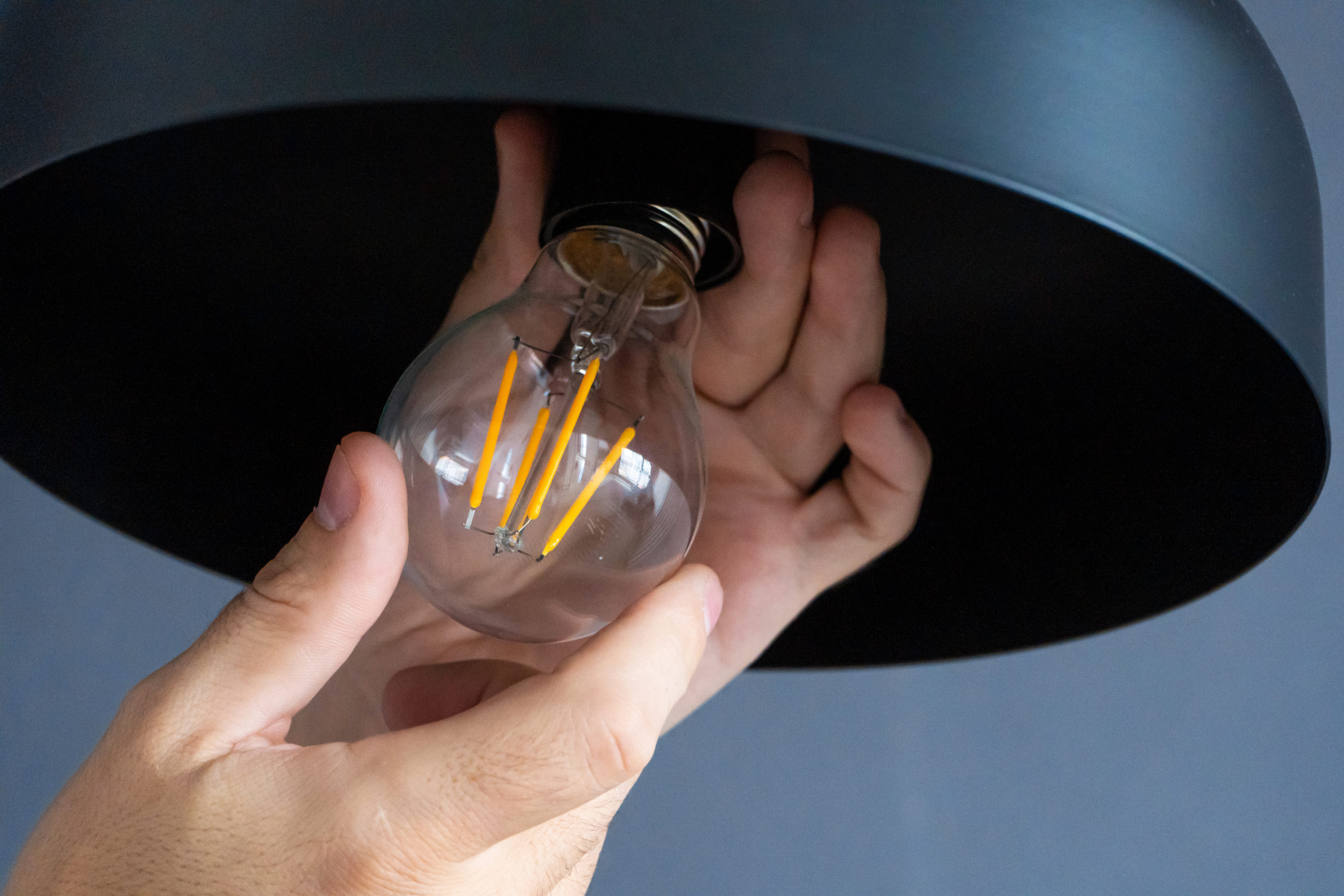 Close-up. A hand changes a light bulb in a stylish loft lamp. Spiral filament lamp.