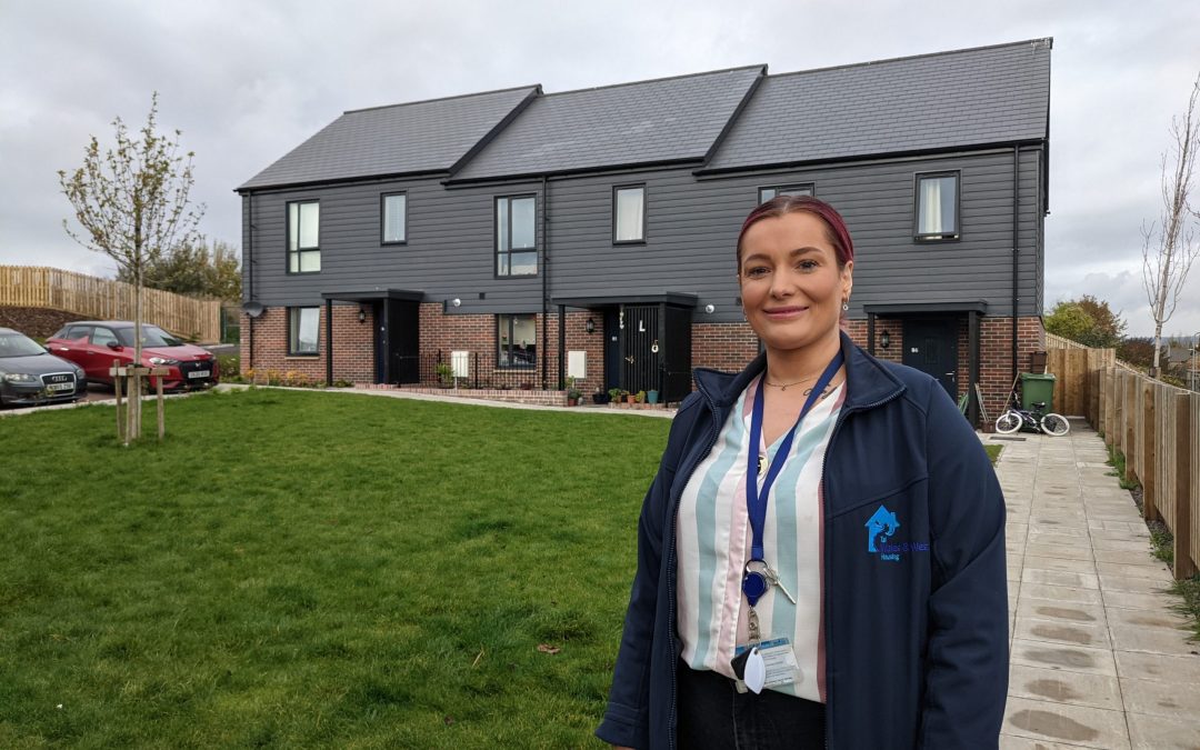 WWH Housing Officer in front of three properties smiling to camera