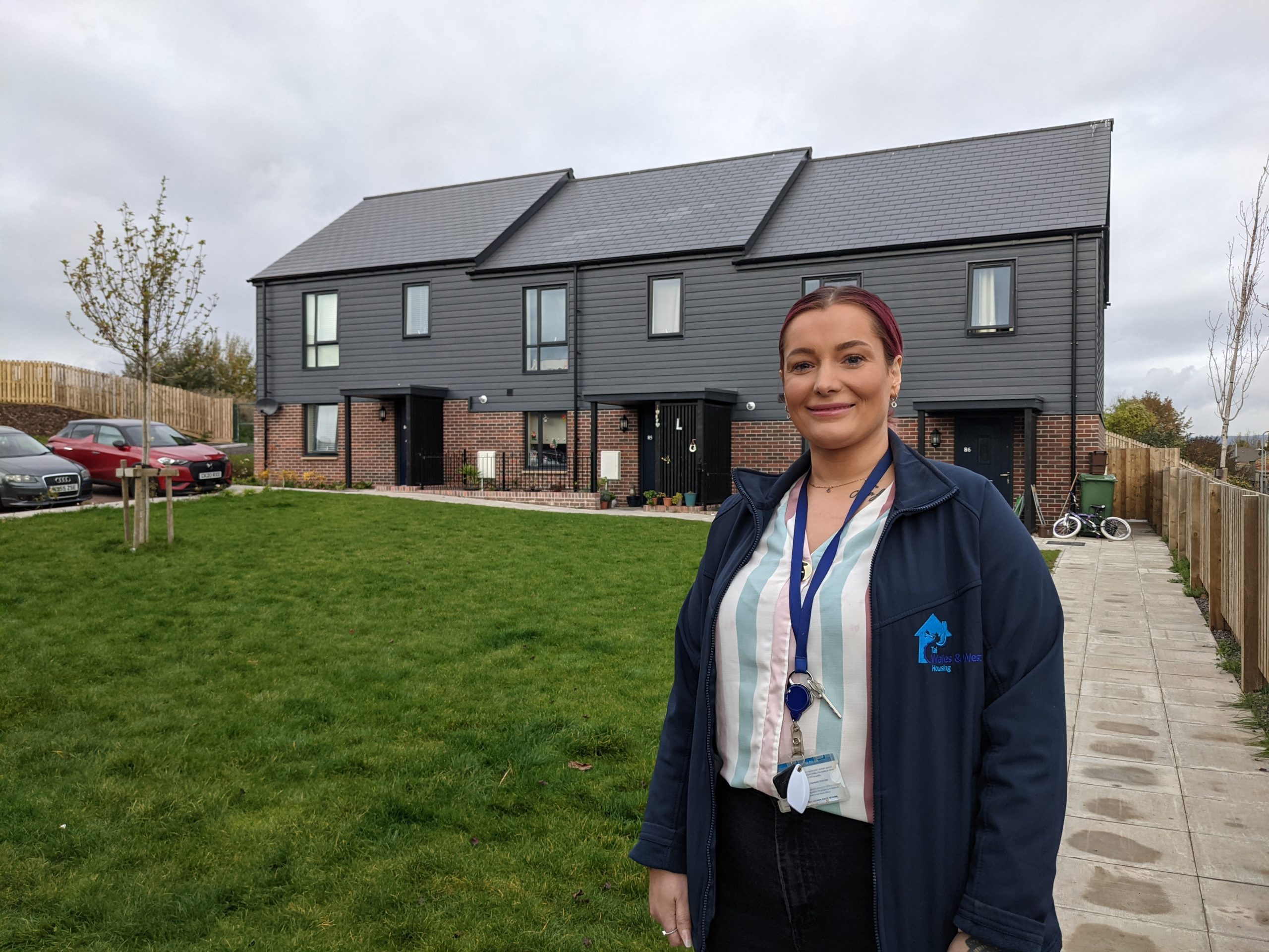 WWH Housing Officer in front of three properties smiling to camera