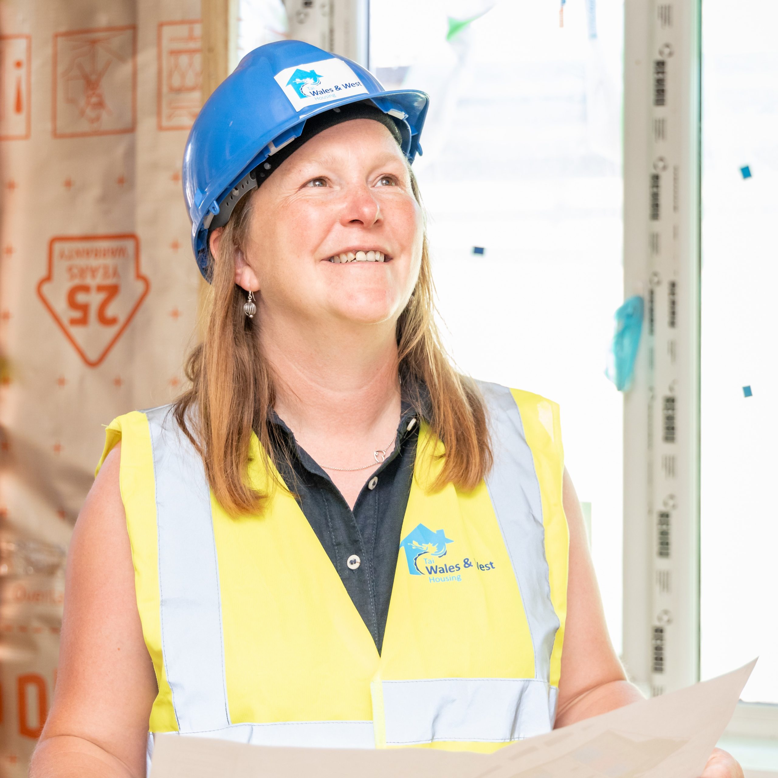 WWH staff member wearing PPE on construction site smiling holding architectural plans